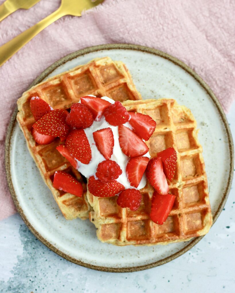 Sunde morgenmadsvafler med havregryn og skyr set ovenfra, toppet med skyr og friske jordbær på en lysegrå tallerken