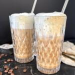 To glas hjemmelavet iskaffe med vaniljeis og luftigt mælkeskum i høje krystalglas med metalsugerør på mørk marmorbaggrund med kaffebønner