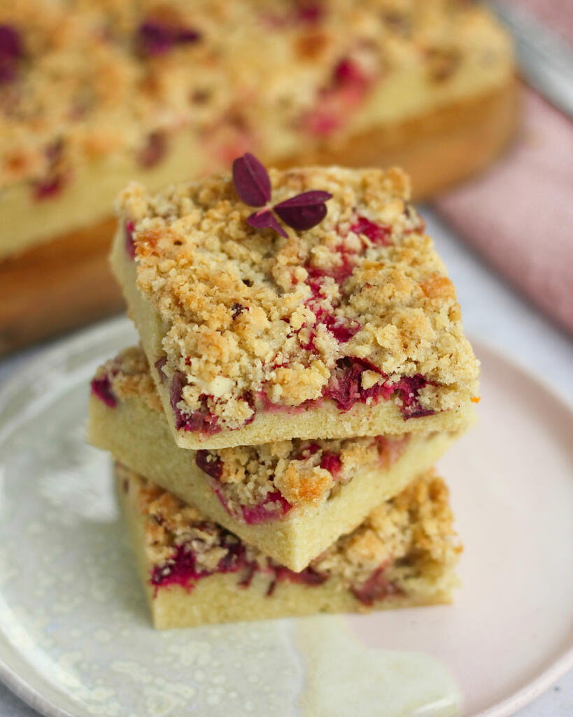 Tre stykker rabarberkage med crumble stablet oven på hinanden på en lyserød tallerken