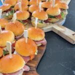 Nærbillede af kolde sliders med parmaskinke, mozzarella og rød pesto pyntet med bambusspyd som mad til gæster