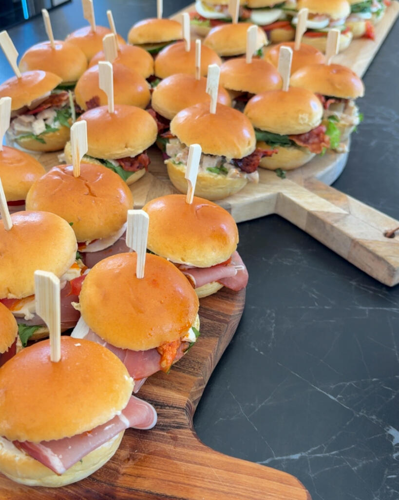 Nærbillede af kolde sliders med parmaskinke, mozzarella og rød pesto pyntet med bambusspyd som mad til gæster
