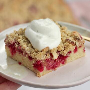 Stykke hindbær crumble kage med svampet bund, saftige hindbær og sprød crumble topping serveret med vaniljecreme fraiche