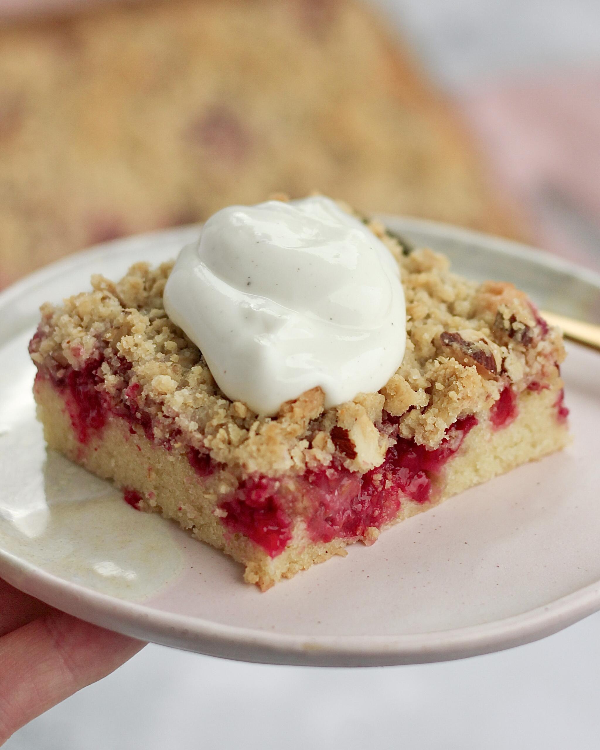 Stykke hindbær crumble kage med svampet bund, saftige hindbær og sprød crumble topping serveret med vaniljecreme fraiche