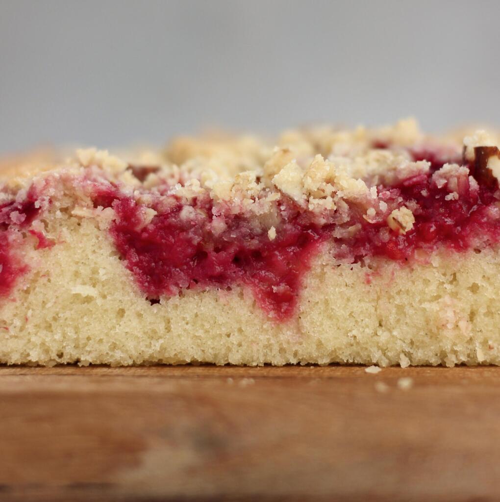Tværsnit af hindbær crumble kage med tydelige lag af svampet kagebund, saftige hindbær og gylden crumble af havregryn og mandler