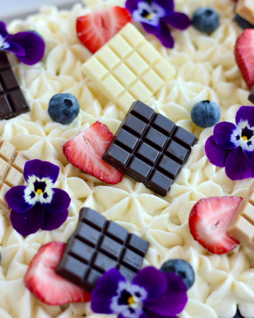 Nærbillede af luftig cream cheese frosting med Callebaut Napolitains chokoladebarer, friske jordbær og stedmoderblomster på svampet chokoladekage