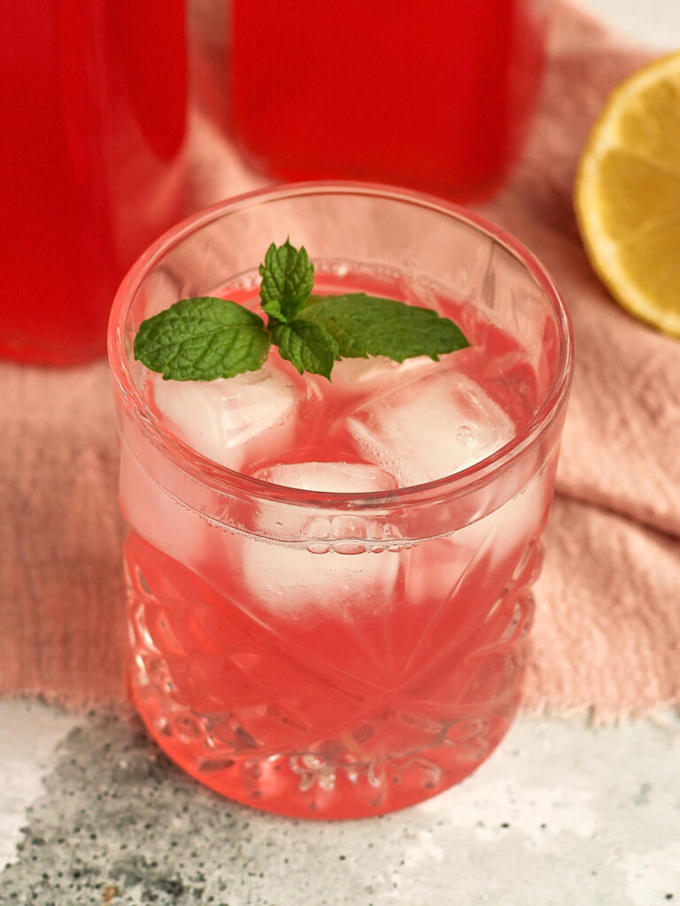 Hjemmelavet rabarbersaft serveret i glas med isterninger og frisk mynte ved siden af flasker med rabarbersaft og citron