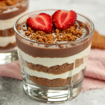 Biscoff cheesecake i glas med lag af knuste Biscoff kiks, cheesecakecreme og chokoladeganache pyntet med to halve jordbær og knuste Biscoff kiks