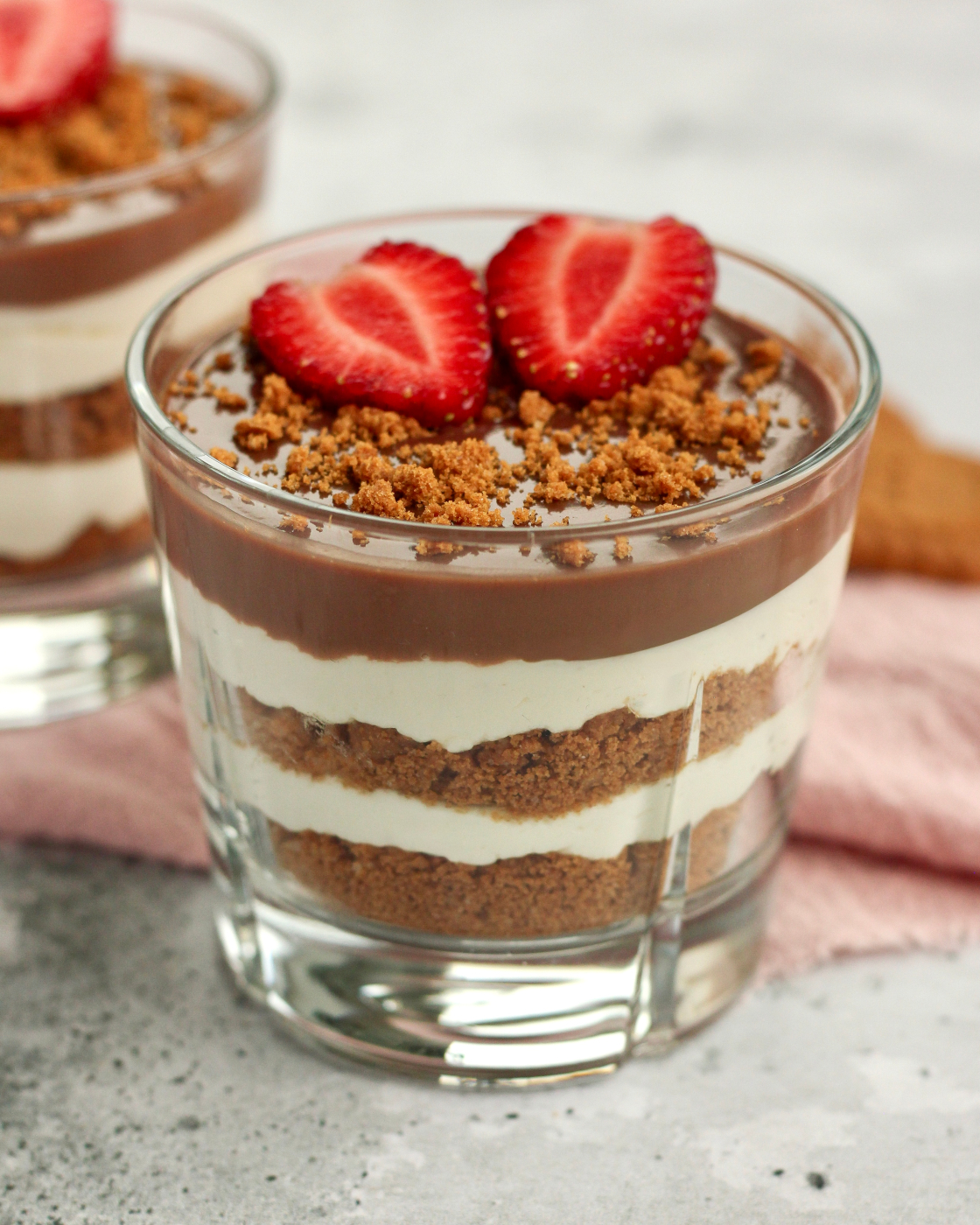 Biscoff cheesecake i glas med lag af knuste Biscoff kiks, cheesecakecreme og chokoladeganache pyntet med to halve jordbær og knuste Biscoff kiks
