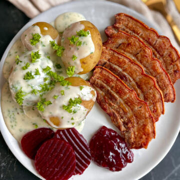 Stegt flæsk med persillesovs, kogte kartofler, rødbeder og tyttebærmarmelade serveret på tallerken