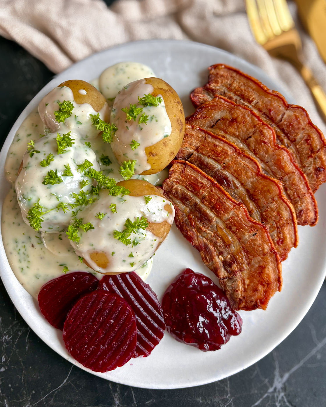Stegt flæsk med persillesovs, kogte kartofler, rødbeder og tyttebærmarmelade serveret på tallerken