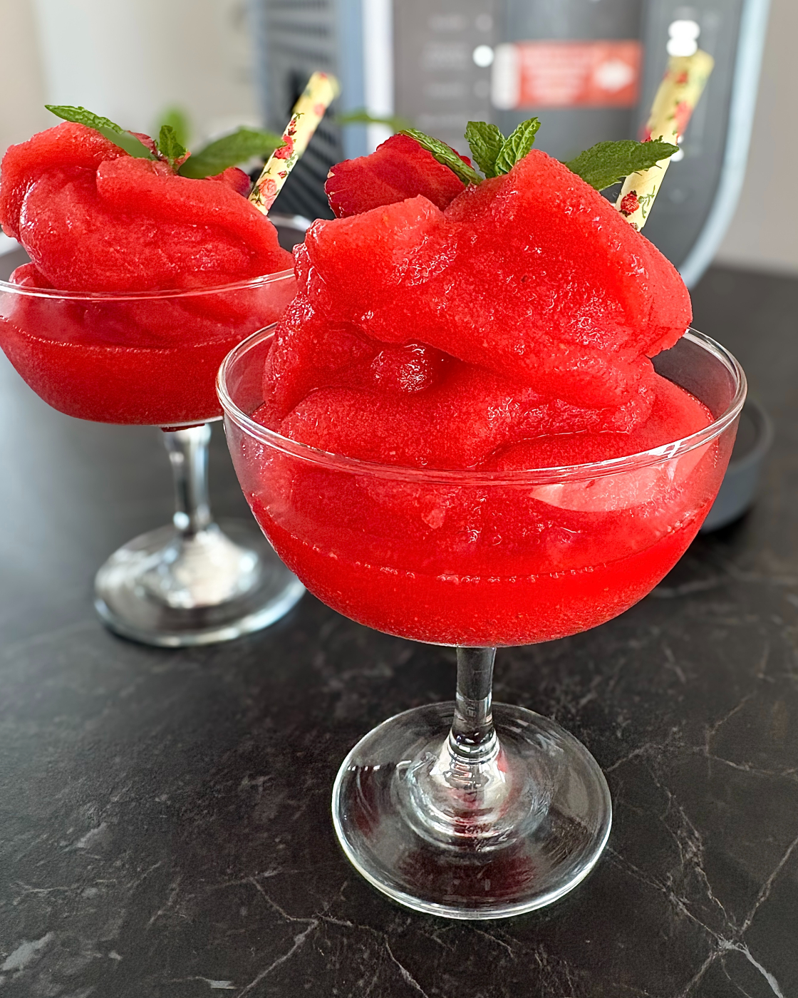 Strawberry daiquiri slush ice i to cocktailglas foran slush ice maskine pyntet med jordbær og mynte
