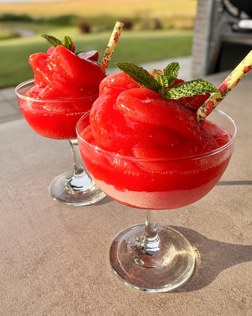 Strawberry daiquiri slush ice i cocktailglas pyntet med friske jordbær, mynte og jordbærsugerør serveret udenfor i solen