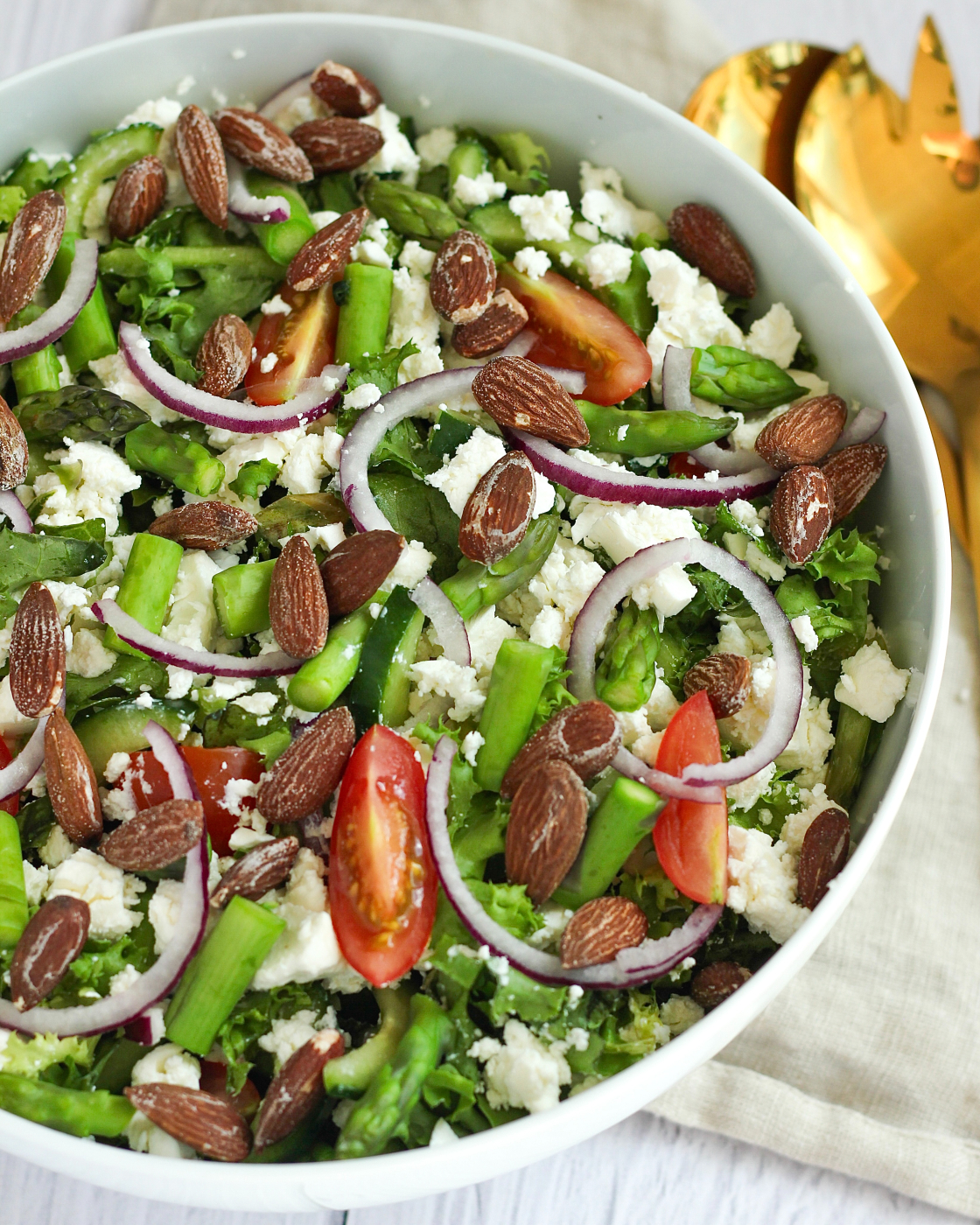 Salat med grønne asparges, feta, cherrytomater, rødløg og saltmandler serveret i hvid skål
