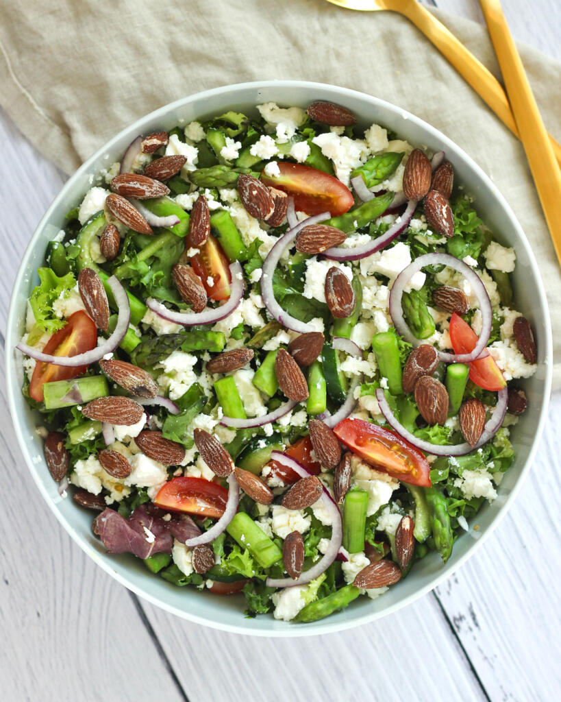 Frisk sommersalat med grønne asparges, feta og cherrytomater i lys skål med guldbestik