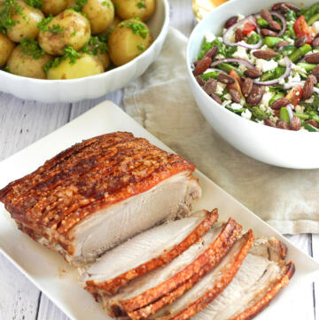 Sommer flæskesteg med sprøde svær serveret med nye kartofler med persillesmør og salat med asparges, feta og cherrytomater