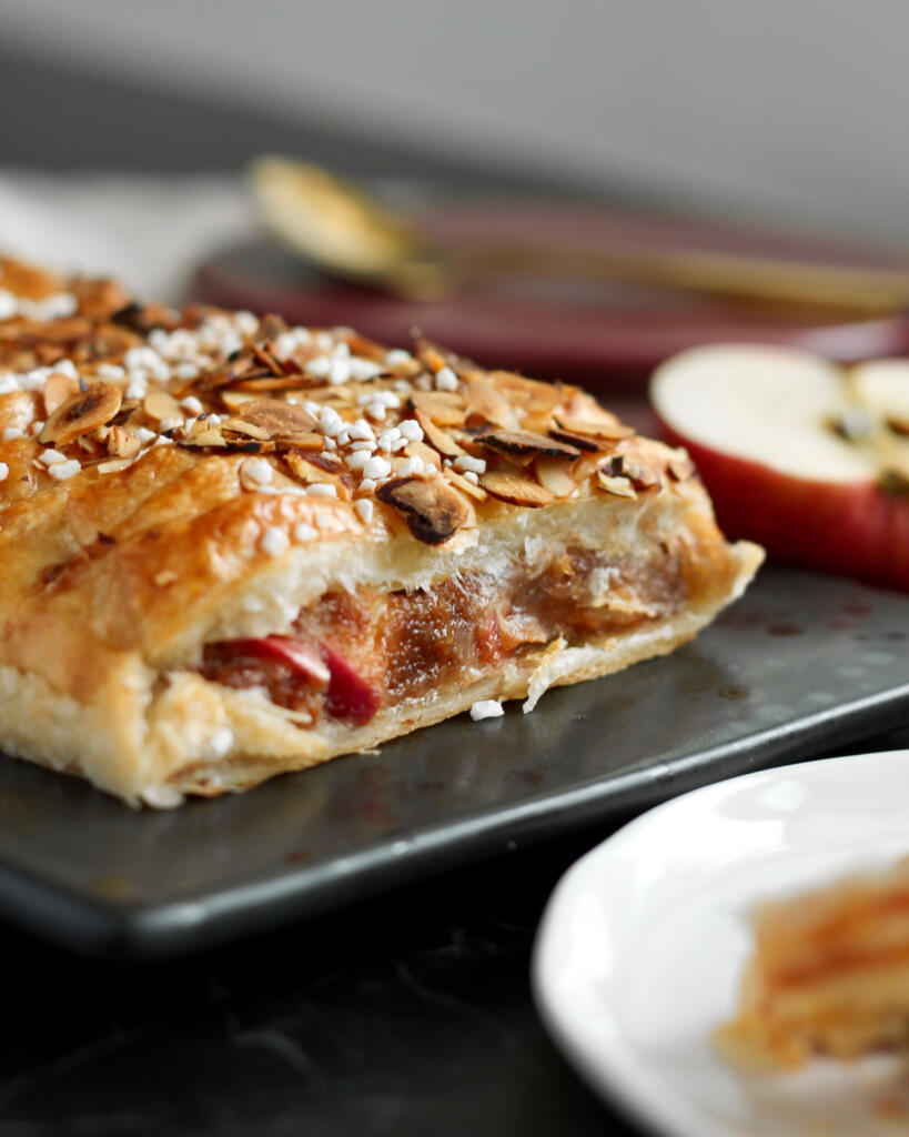 Nem kringle med æbler toppet med ristede hasselnøddeflager og perlesukker med et halvt æble ved siden af