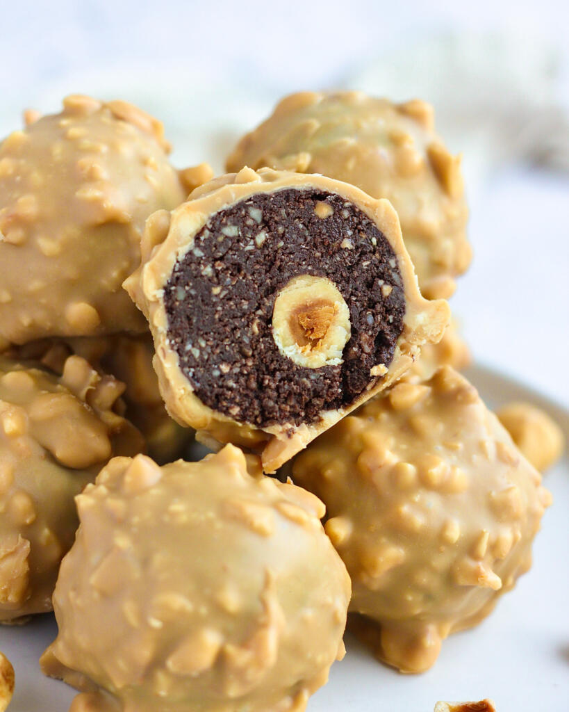 Nærbillede af hjemmelavet Ferrero Rocher skåret over med mørkt hasselnøddefyld, en hel hasselnød i midten og overtræk af karamelchokolade