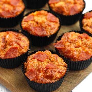 Pizza muffins med pepperoni og gylden cheddar i sorte muffinforme på træskærebræt