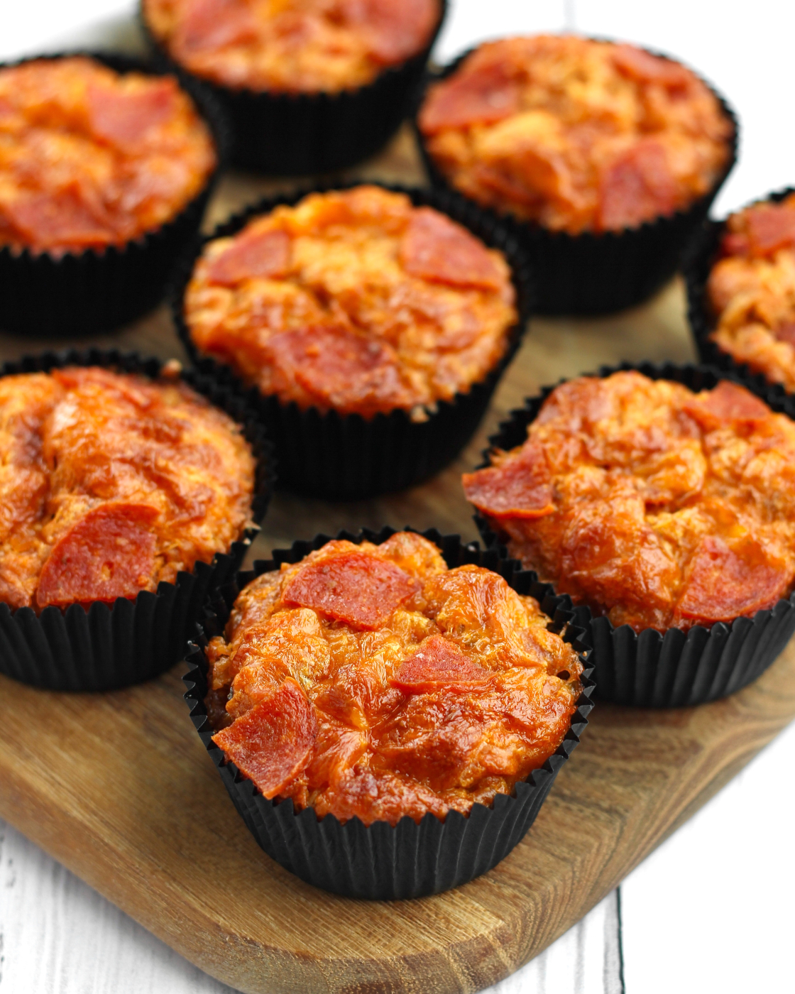 Pizza muffins med pepperoni og gylden cheddar i sorte muffinforme på træskærebræt