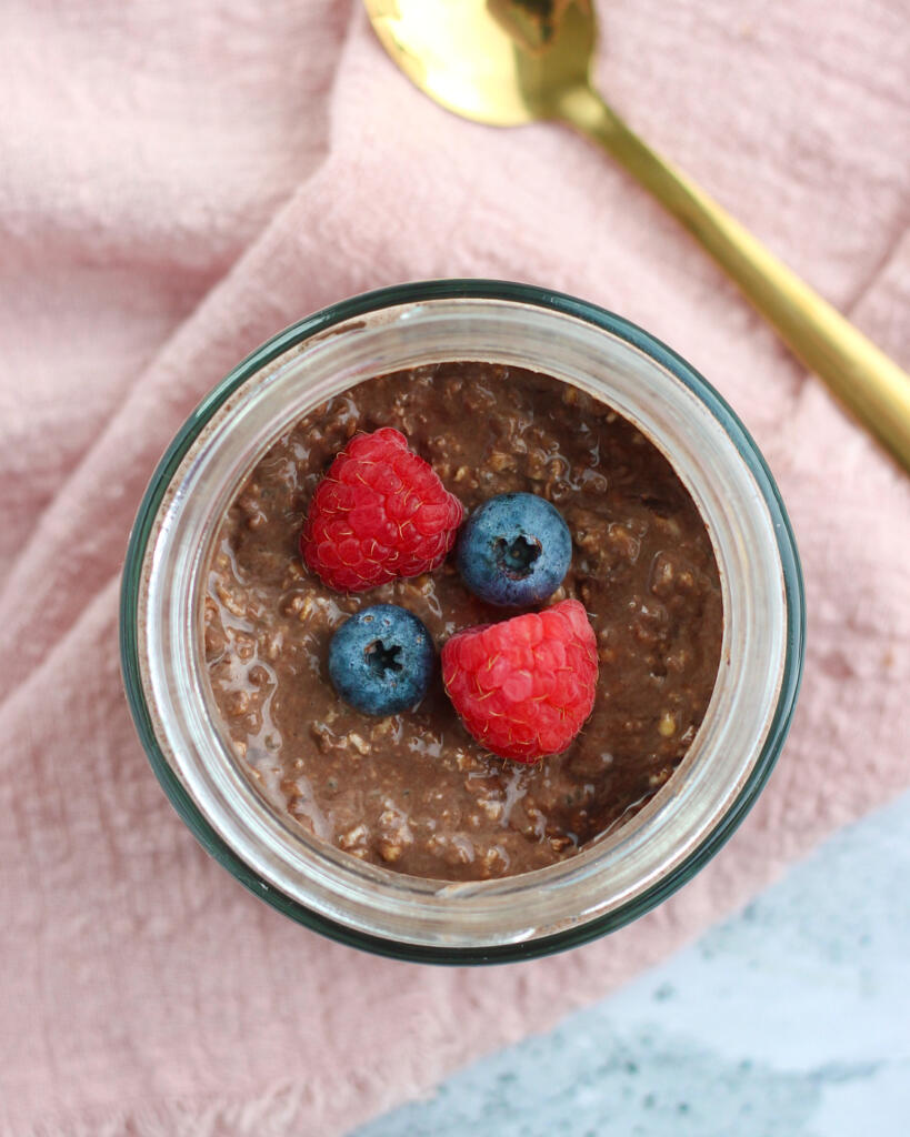 Overnight oats med kakao og skyr set oppefra i glas med friske bær og en guldteske ved siden af