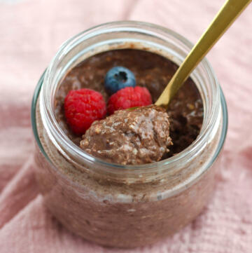Overnight oats med kakao i glas toppet med hindbær og blåbær med en guldske fuld af cremet chokoladegrød