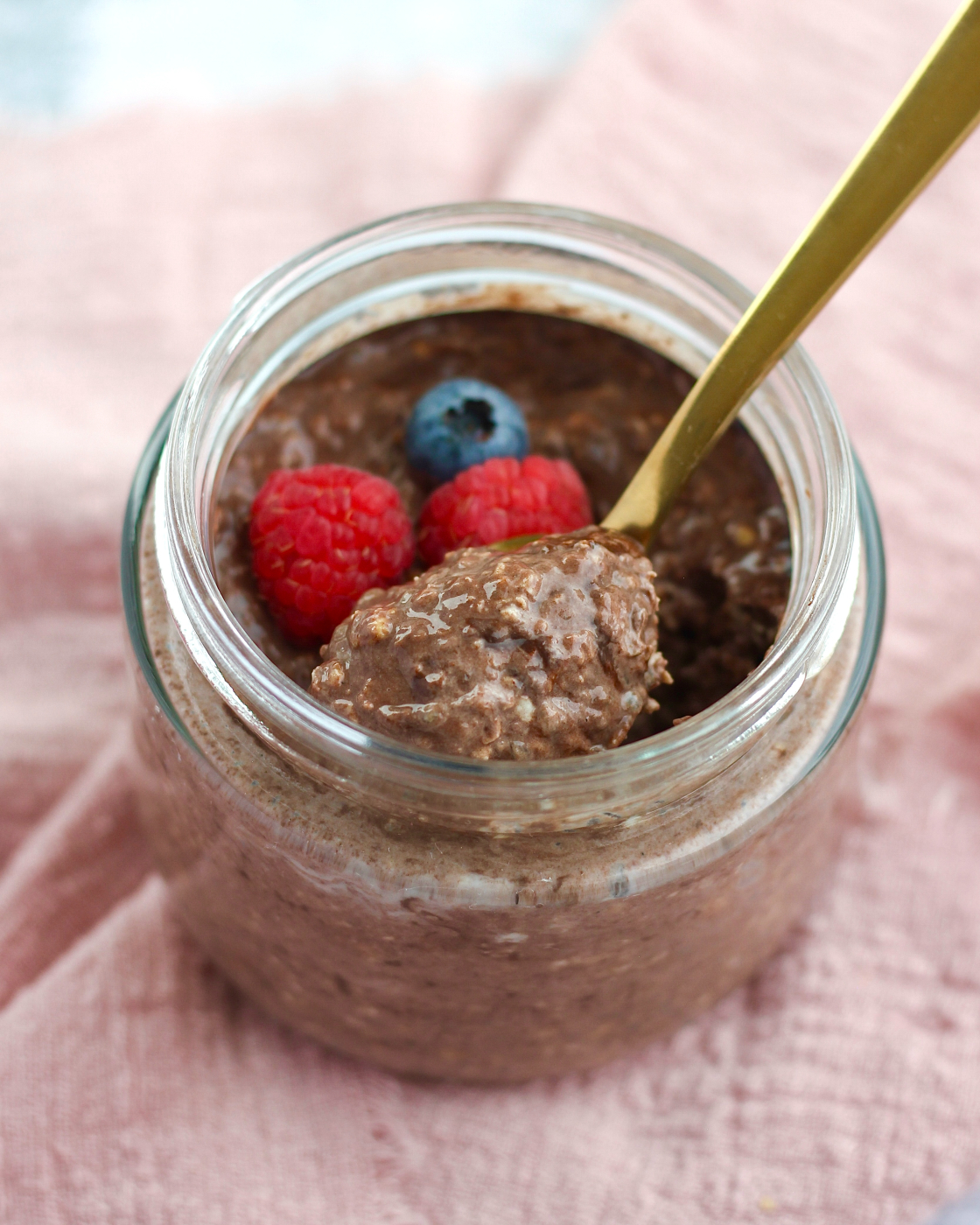 Overnight oats med kakao i glas toppet med hindbær og blåbær med en guldske fuld af cremet chokoladegrød