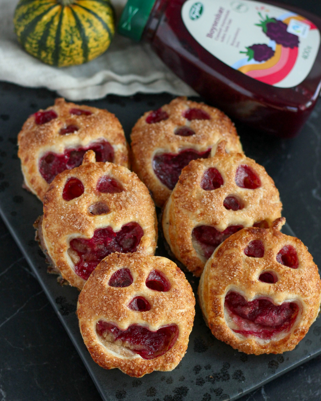 Små Halloween tærter formet som græskar med ansigter af butterdej, fyldt med marcipan og boysenbærmarmelade og drysset med kanelsukker