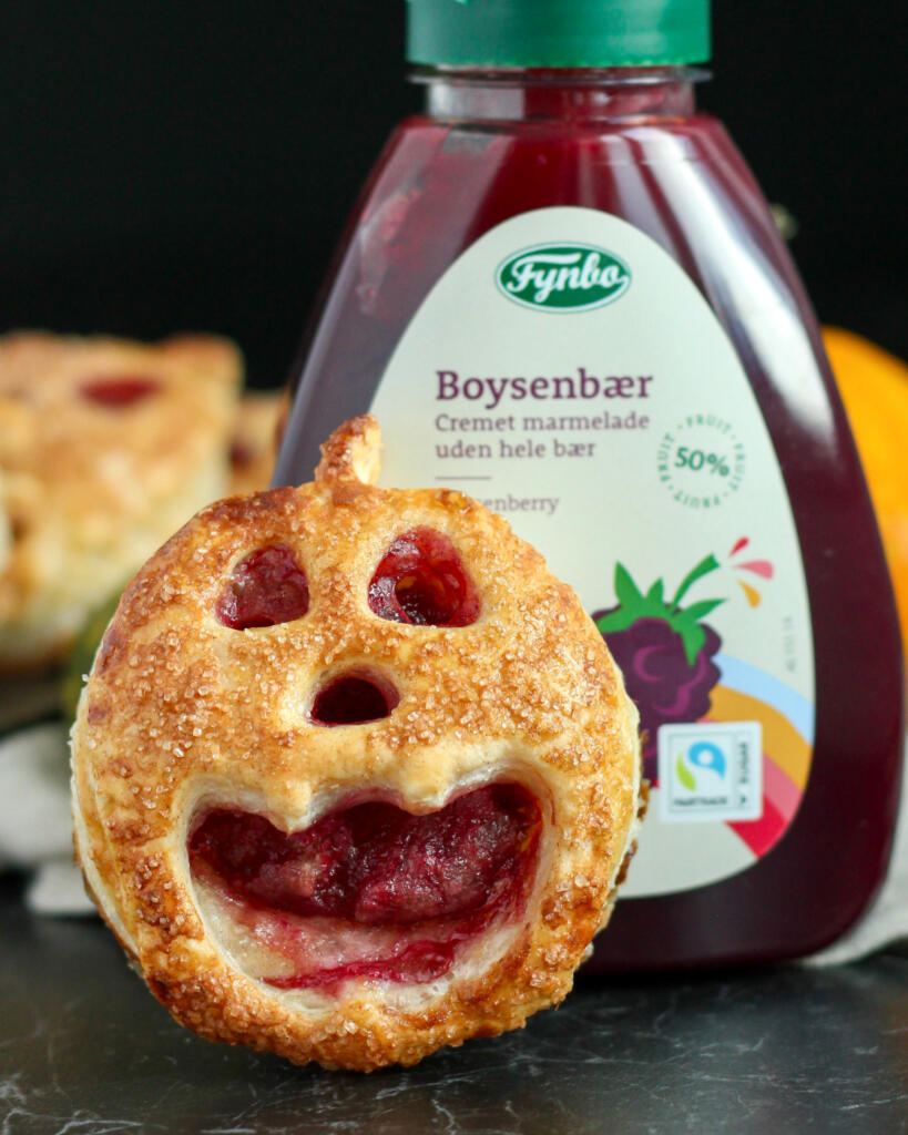 Nærbillede af Halloween tærte af butterdej formet som et græskar med udstukket ansigt og rødt fyld af boysenbærmarmelade