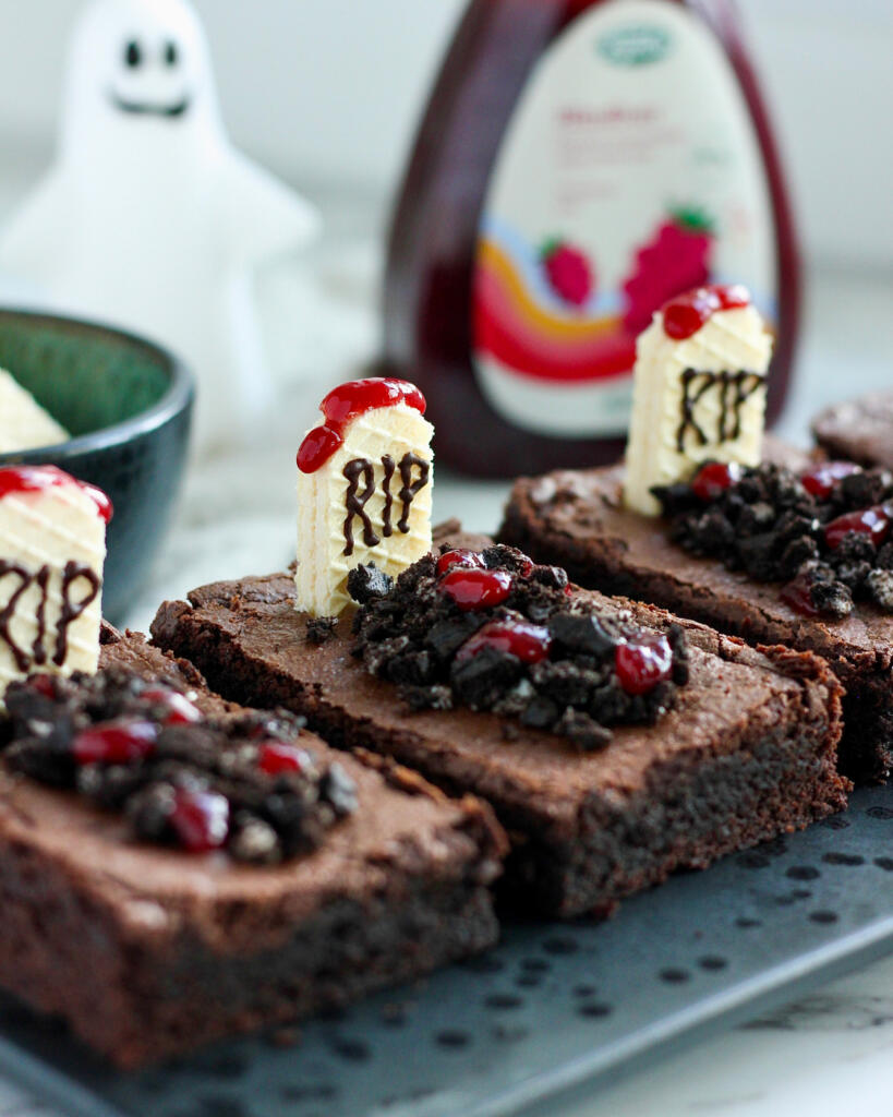 Nærbillede af fudgy Halloween brownie med vaffelgravsten, kakaokiks som jord og hindbærmarmelade som blod