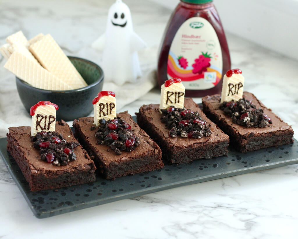 Fire Halloween brownies pyntet som gravsteder med vaffelgravsten, knuste kakaokiks og hindbærmarmelade på sort fad