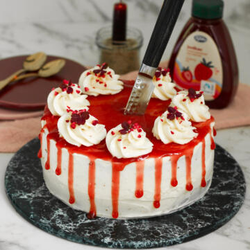 Halloween kage med hvid cream cheese frosting, jordbærmarmelade der drypper ned ad siderne som blod og en kniv stukket ned i midten