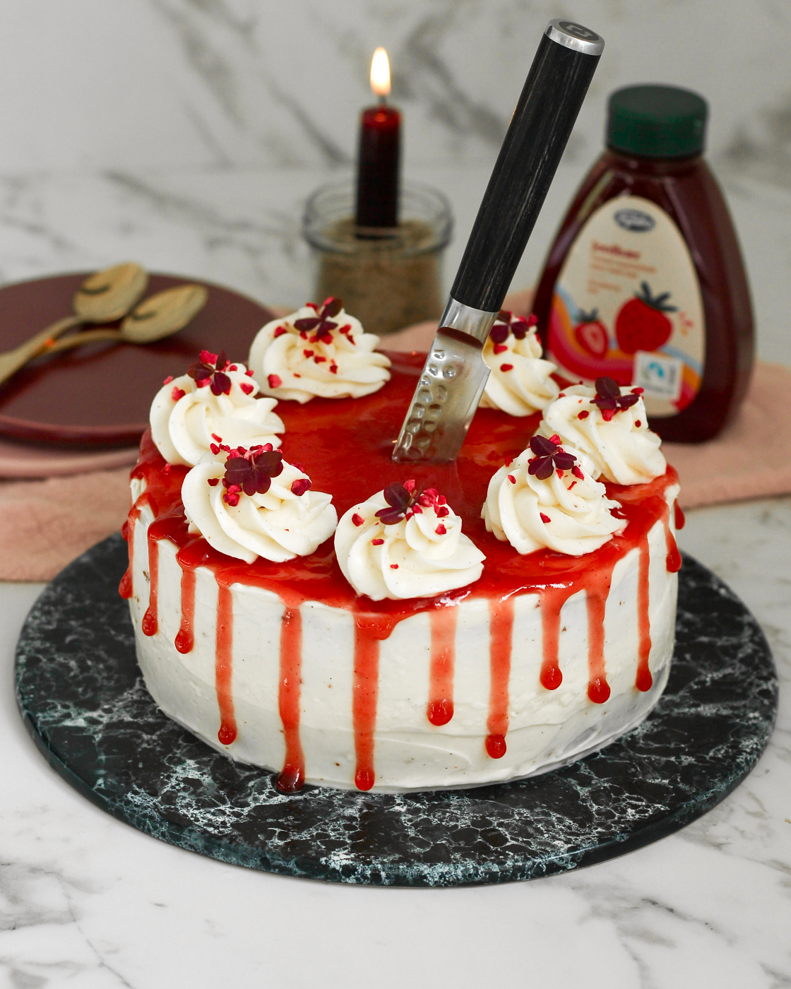 Halloween kage med hvid cream cheese frosting, jordbærmarmelade der drypper ned ad siderne som blod og en kniv stukket ned i midten