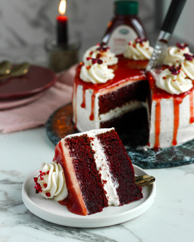 Stykke blodig Halloween kage med to lag dybrød red velvet bund, cream cheese frosting og jordbærmarmelade som blod