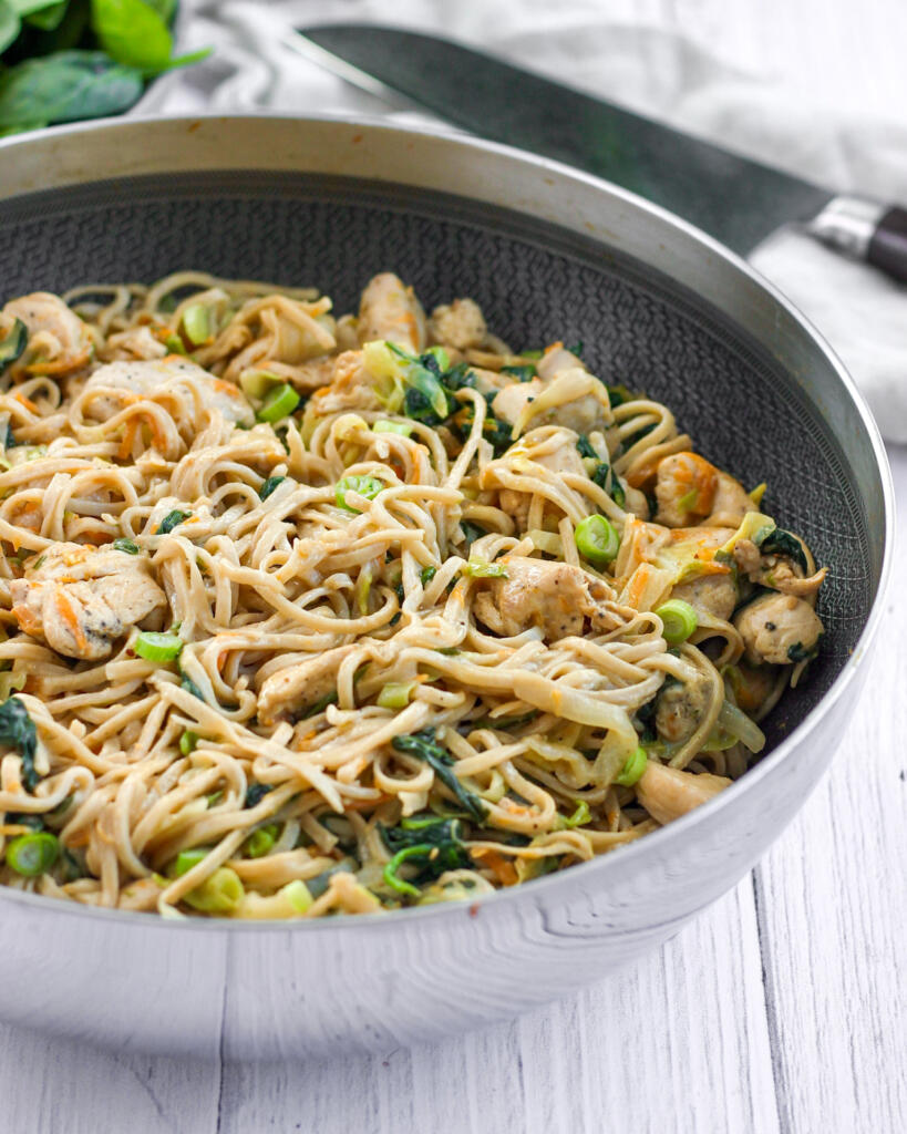 Cremet wok med kylling og nudler med spinat, spidskål og forårsløg i en wokpande